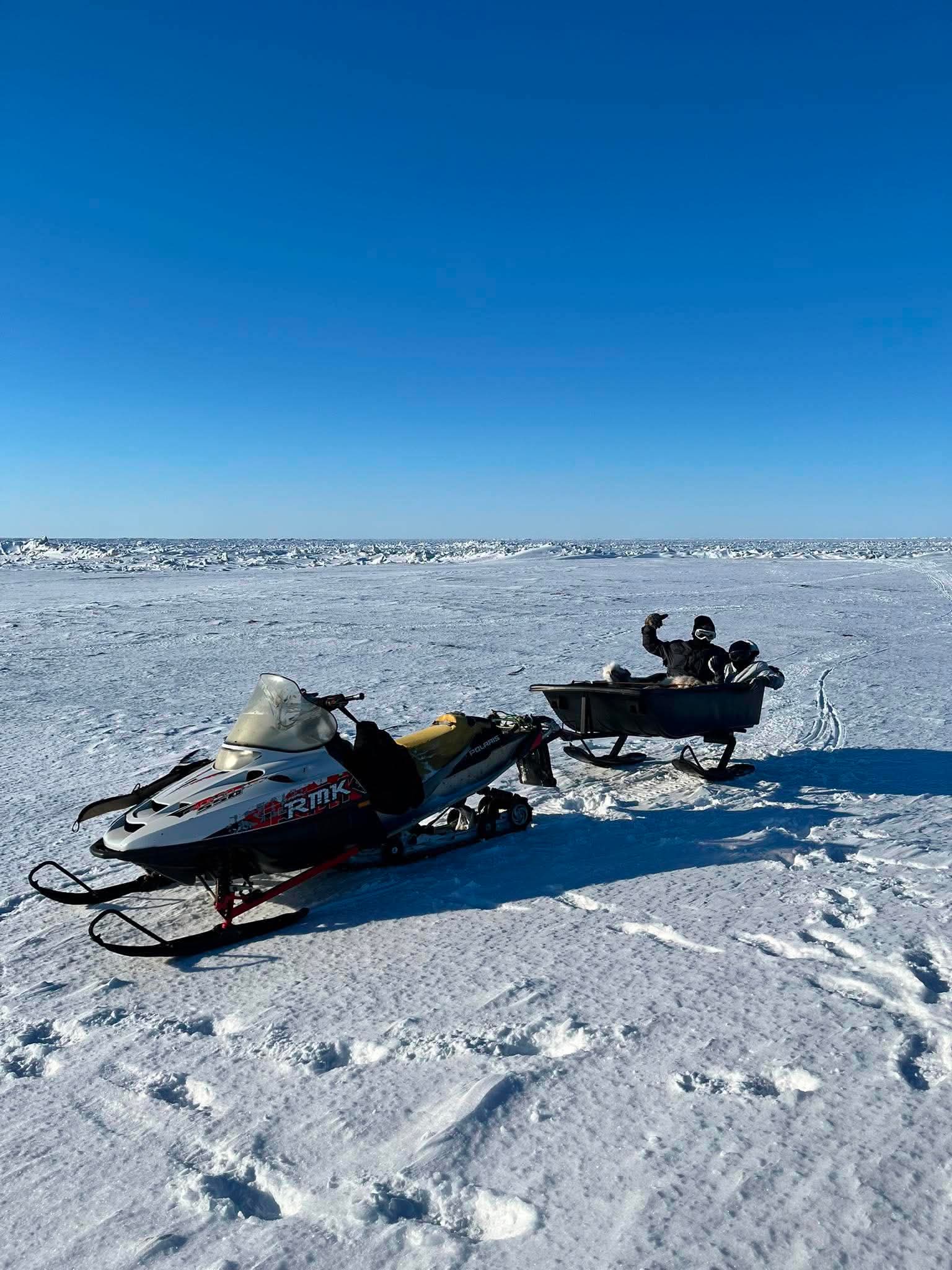 Two guests riding in a ski sled pulled by a snowmachine on the winter route to Point Barrow