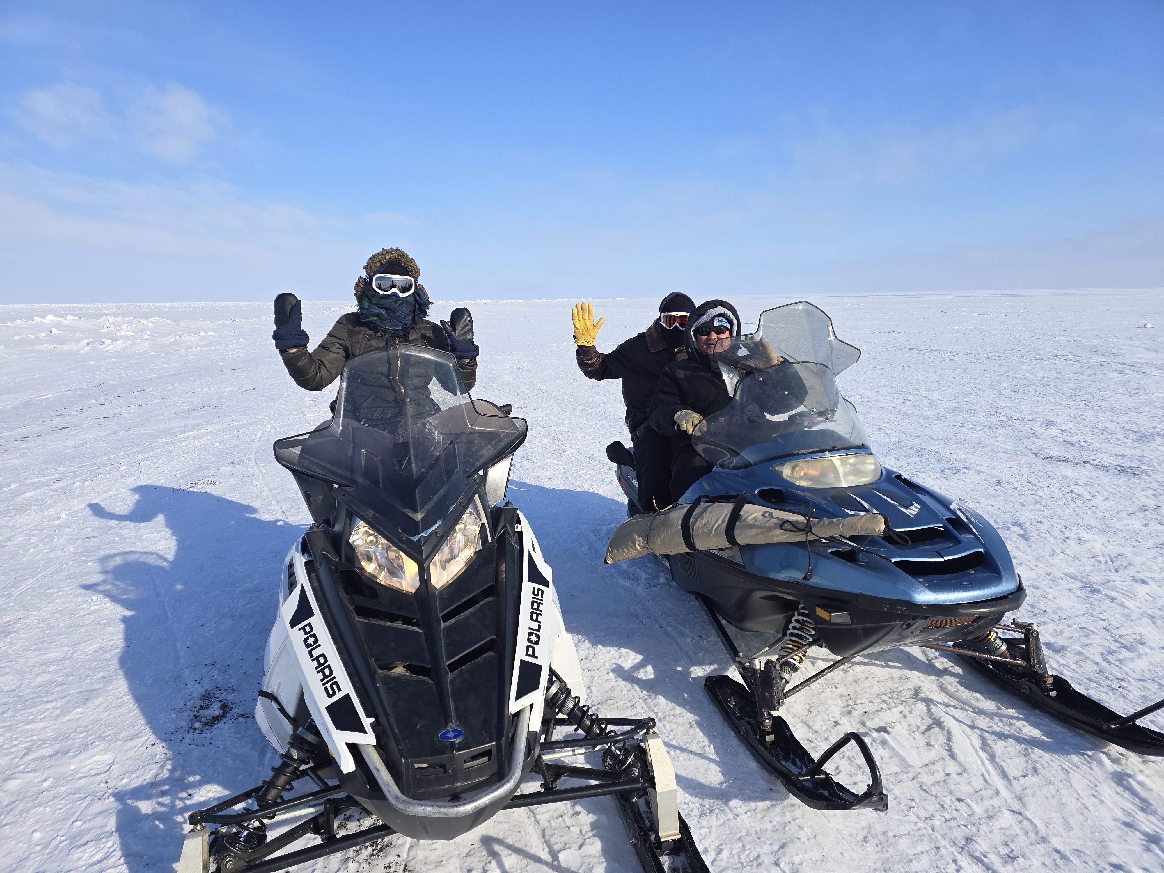 Two guests riding as passengers on snowmachines during a winter Point Barrow tour with Kiita Tours