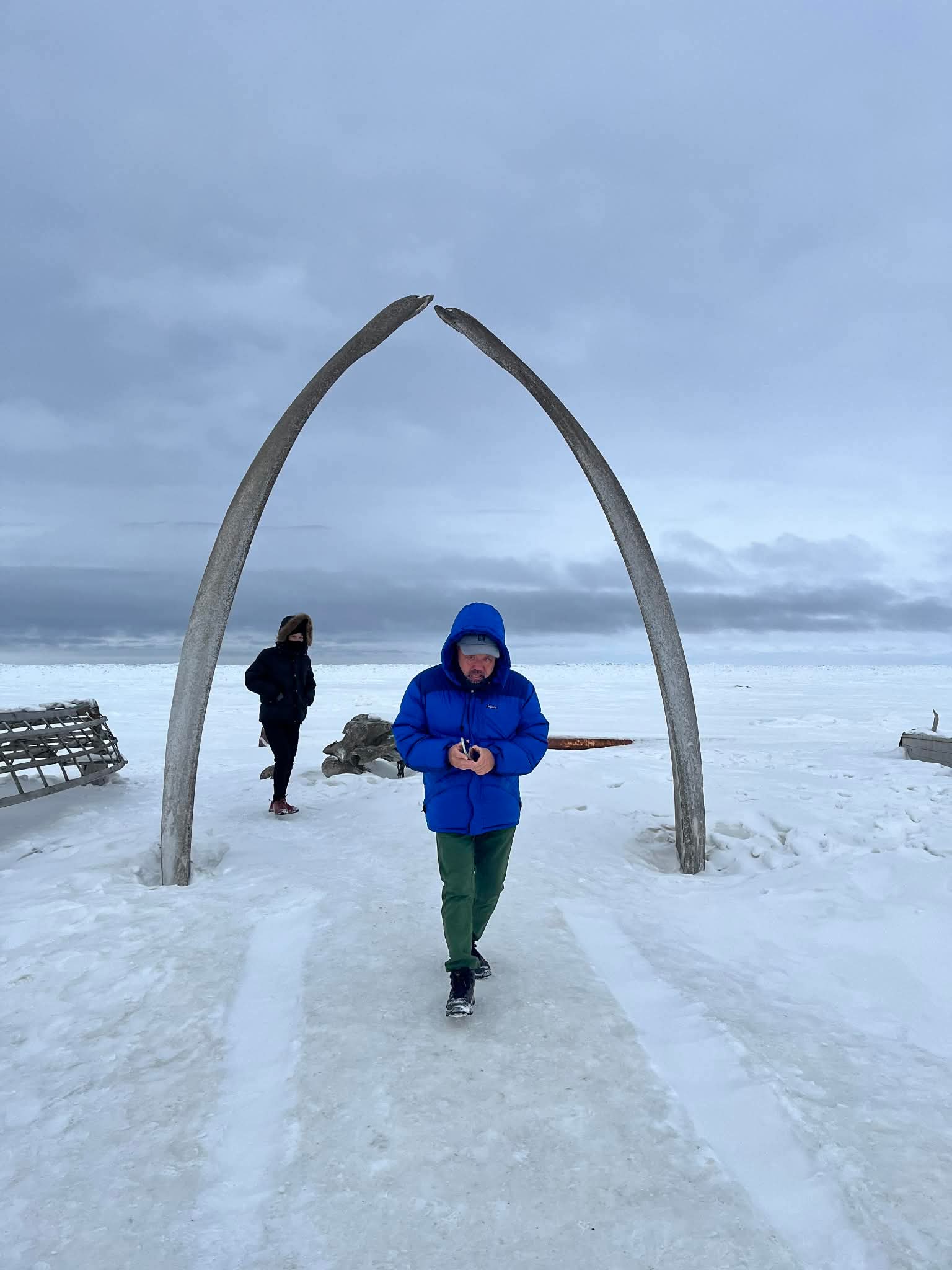 Two guests walking through the Whalebone Arch in winter, Utqiaġvik, Alaska