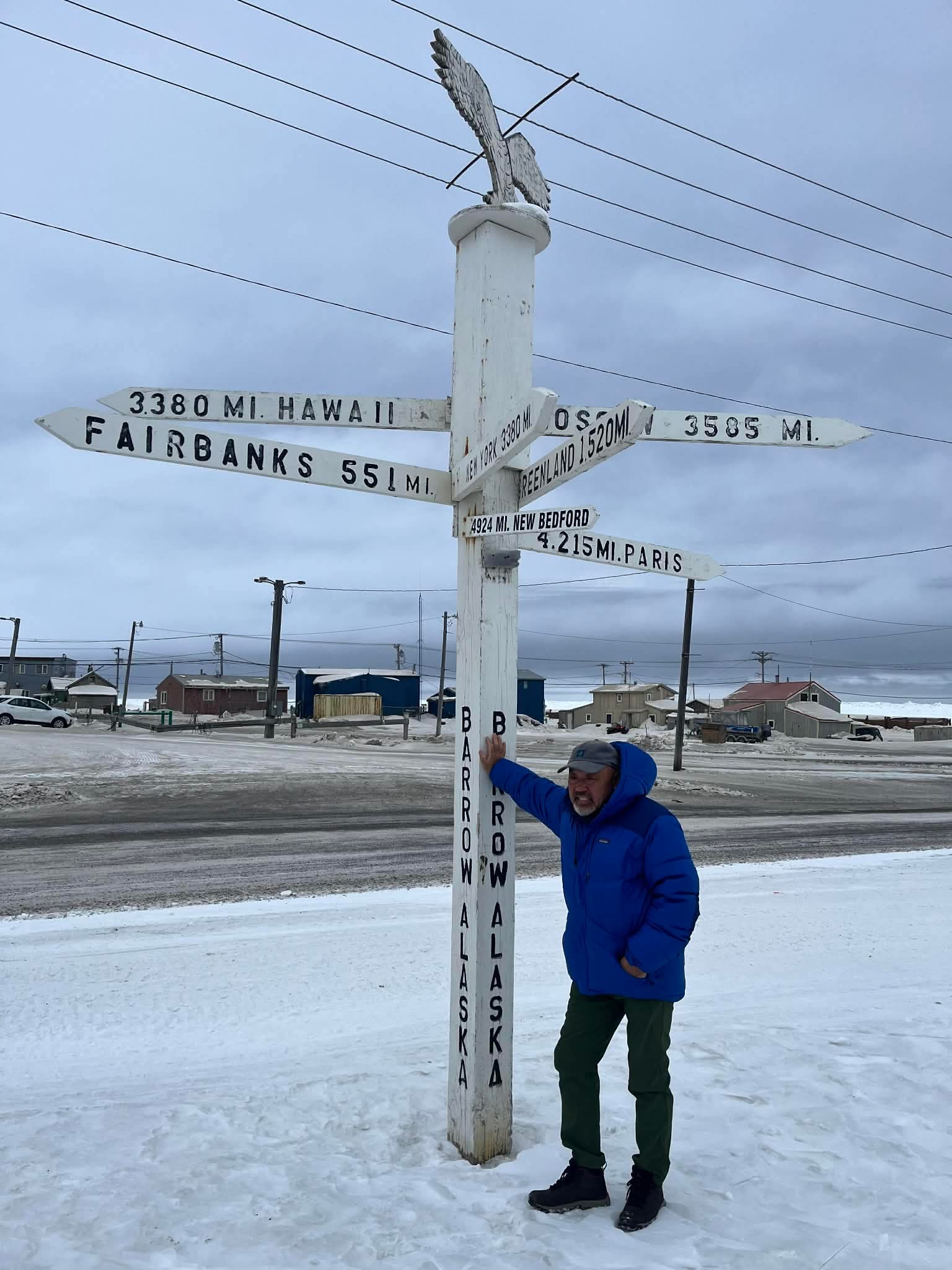 Guest at the Barrow distance crossroads sign showing miles to world cities